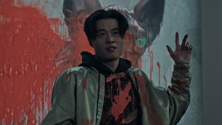 Simon from You standing in front of his artwork, covered in splashed red paint.