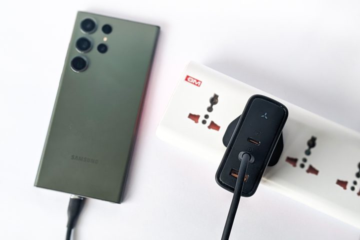 Voltme Revo 140 GaN charger plugged into a power strip and kept alongside a green Samsung Galaxy S23 Ultra on a white background.
