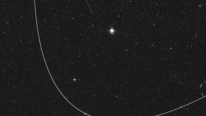 The curving light streak created by an artificial satellite mars an image taken by the Hubble Space Telescope.