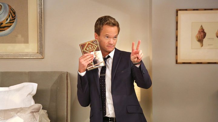 Barney in How I Met Your Mother giving a peace sign and holding a copy of The Bro Code.