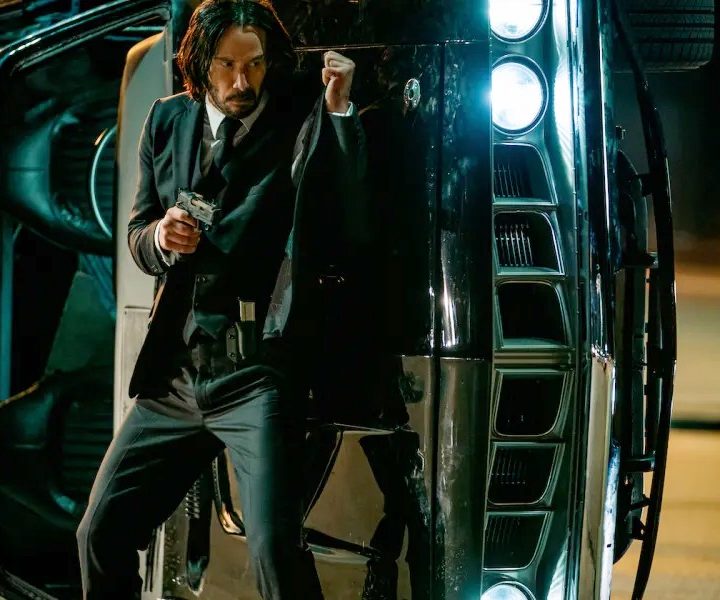 John Wick stands behind a car in John Wick: Chapter 4.