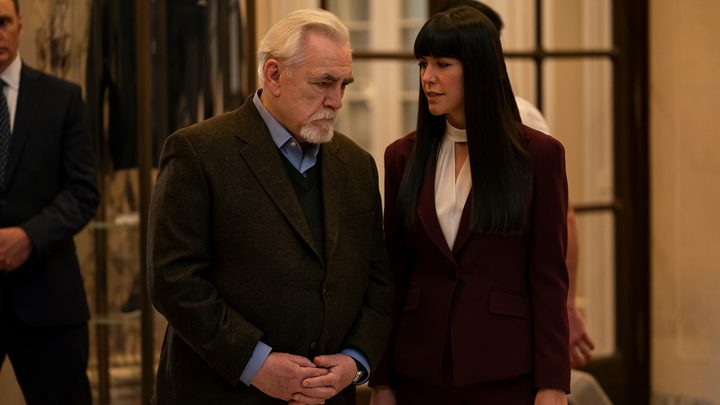 Logan leaning down listening as Kerry says something in his ear in Succession.