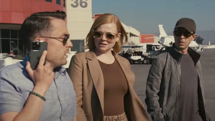 Two men and a woman talk on a runway in Succession.