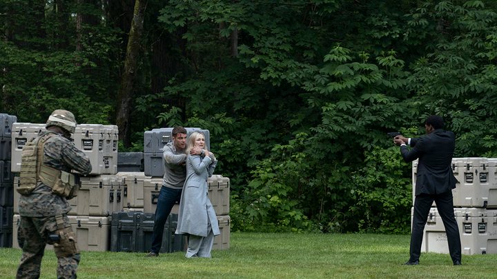 Peter in a field in The Night Agent, holding a gun to President Travers' neck.