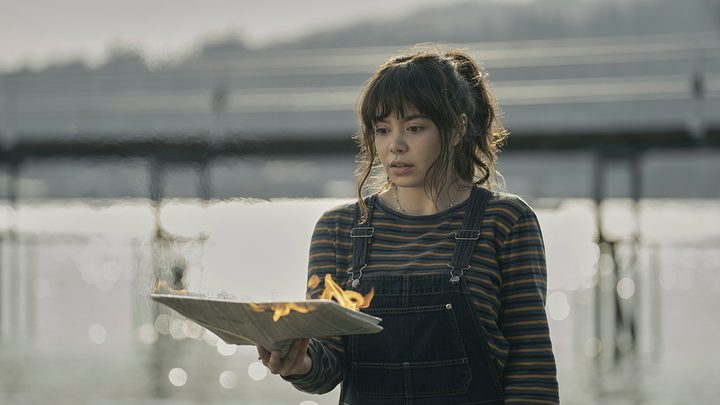 A teenage woman holds a paper that's caught fire in a scene from The Power on Amazon Prime Video.