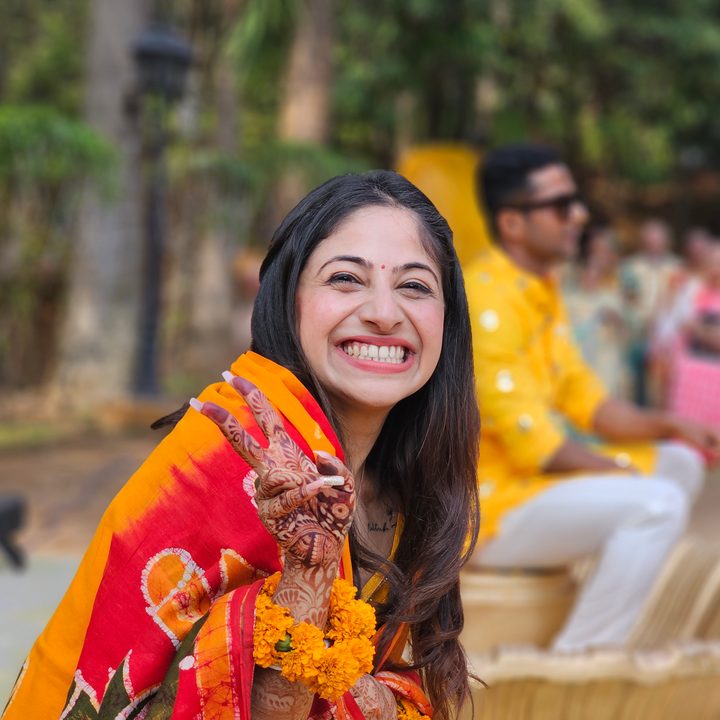 Indian bride smiling and making a victory sign with her hand with groom in the background captured with the Samsung Galaxy S23 Ultra’s 3x telephoto portrait mode camera.