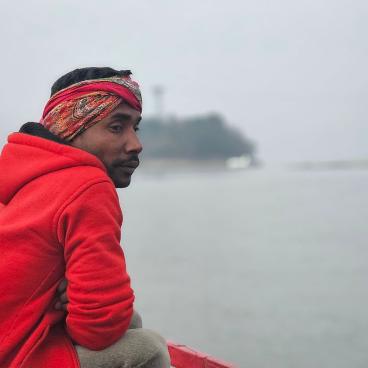 Assistant motor boat operator with an island the Brahmaputra river in background captured with the Samsung Galaxy S23 Ultra’s 3x telephoto portrait mode camera.