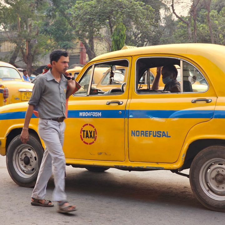 Person walking across a yellow taxi in Kolkata, India, with other taxis in the background captured with the Samsung Galaxy S23 Ultra’s 3x telephoto portrait mode camera.