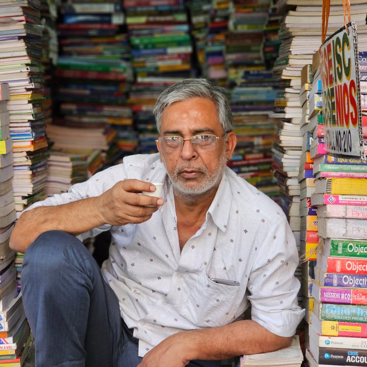 Book seller holding a cup of tea sitting in front of his shop captured with the Samsung Galaxy S23 Ultra’s 3x telephoto portrait mode camera.