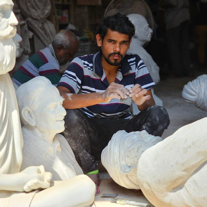 A scultor working on white plaster of paris/clay statues captured with the Samsung Galaxy S23 Ultra’s 3x telephoto portrait mode camera.