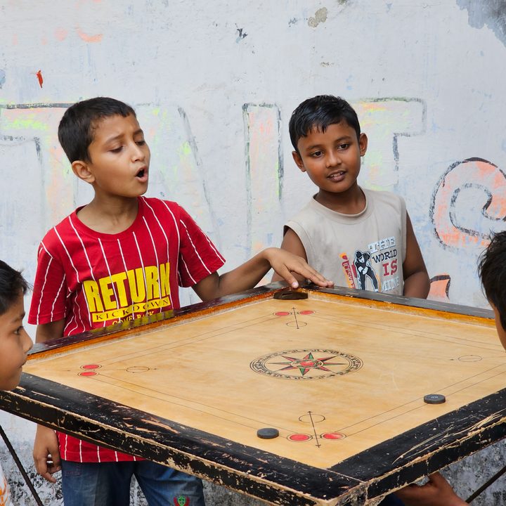 Kids standing on four sides of a carom board captured with the Samsung Galaxy S23 Ultra’s 3x telephoto portrait mode camera.