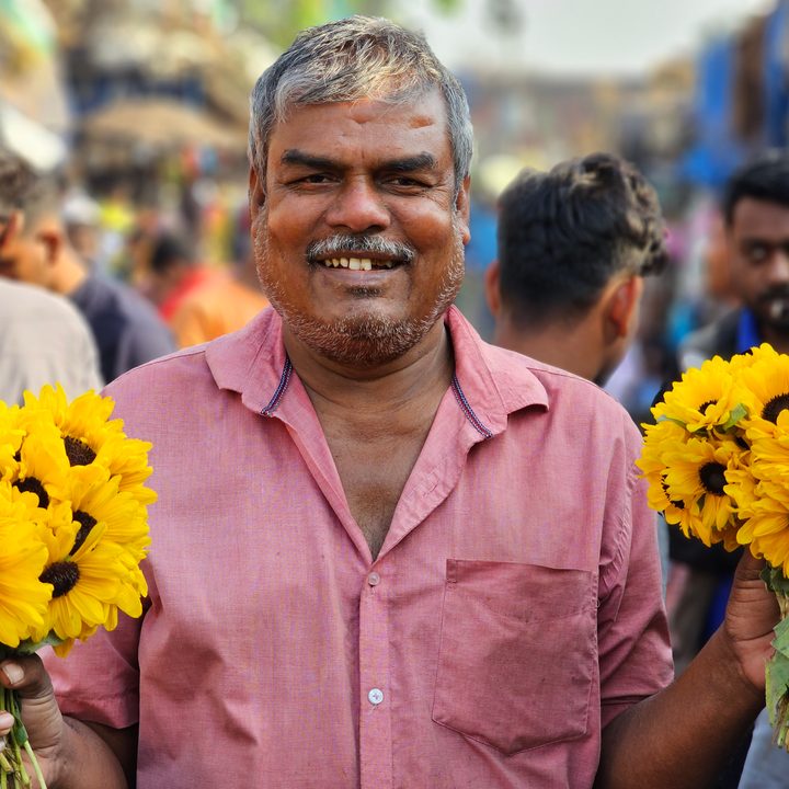 Smiling flower vendor in a flower market captured with the Samsung Galaxy S23 Ultra’s 3x telephoto portrait mode camera.