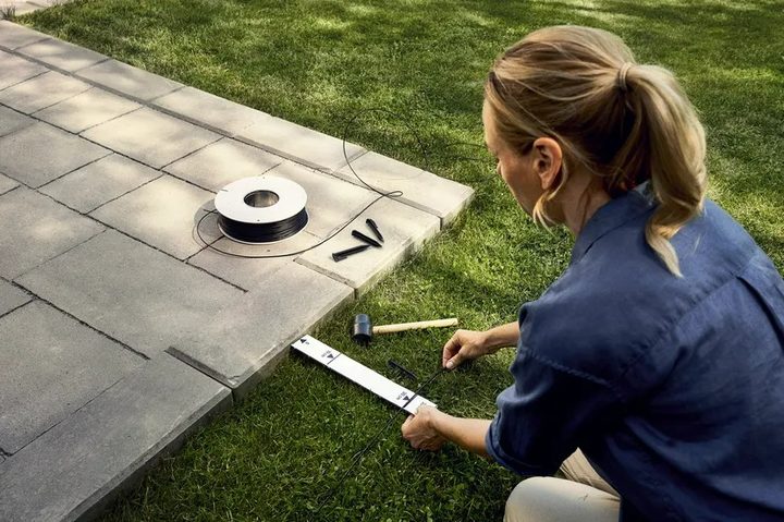 A person installing a boundary wire for a Husqvarna product.