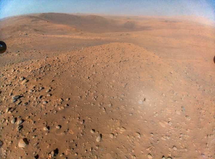 An image of Mars taken from the air by the ingenuity helicopter, with the Perseverance rover visible in the top left.