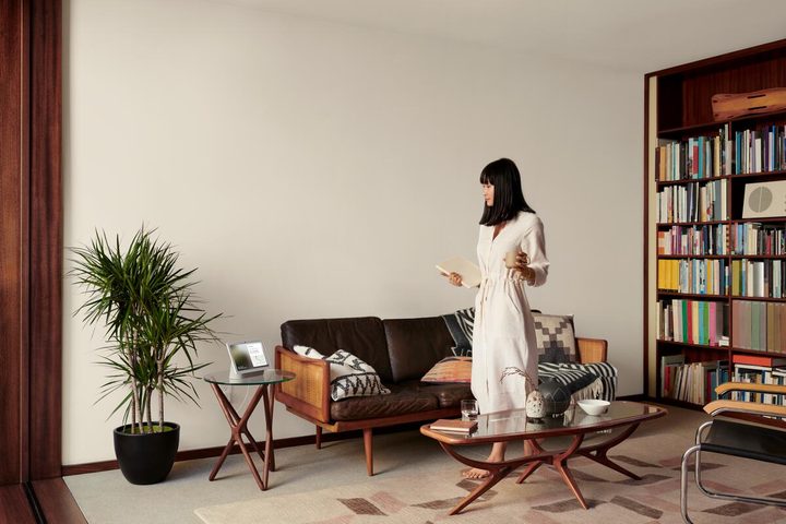A person standing in a living room while looking at a Google device.