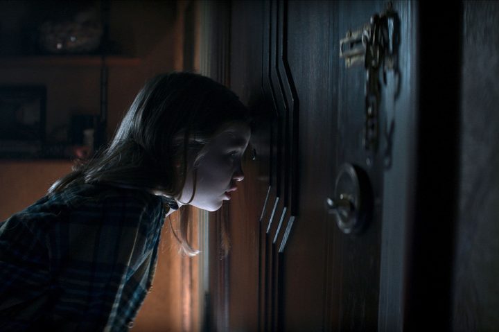 Kassie looks through a door's peephole in Evil Dead Rise.