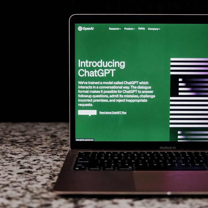 The ChatGPT website on a laptop's screen as the laptop sits on a counter in front of a black background.