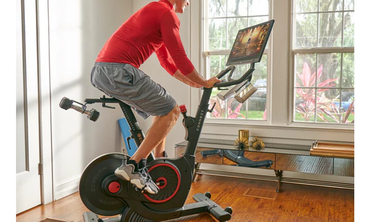 Riding an Echelon Connect Bike EX-5s-22 inside a house with a view of flowering bushes.