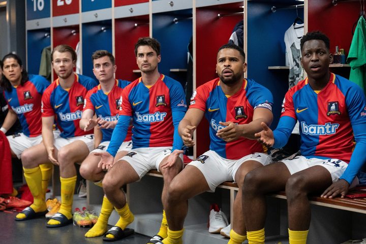 Soccer players sit on a bench in Ted Lasso season 3.