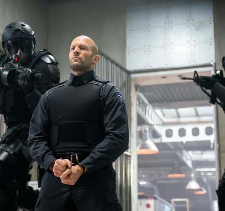 Jason Statham sits, handcuffed, in front of two guards in Wrath of Man.