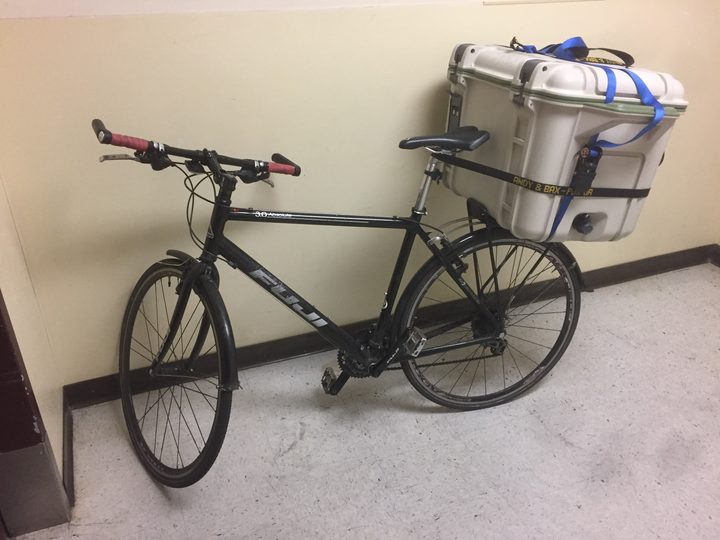 A bicycle with a cooler strapped to the back sits in a lobby.