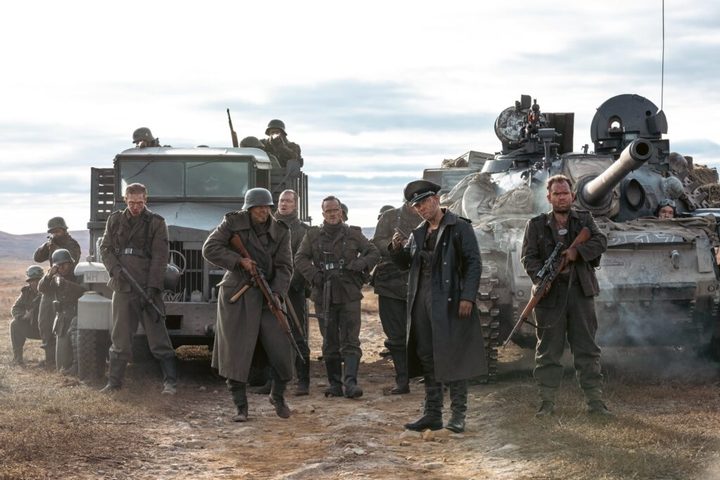 A group of Nazis stand next to 2 trucks in Sisu.