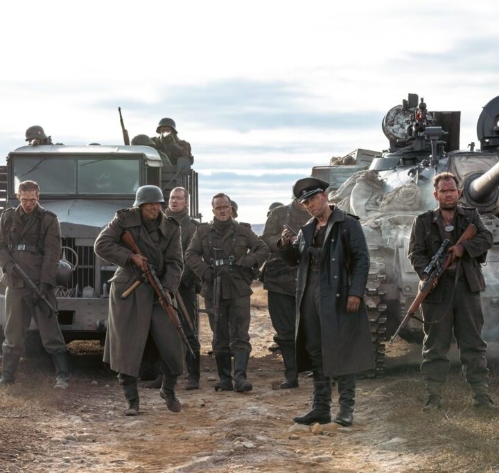 A group of Nazis stand next to 2 trucks in Sisu.