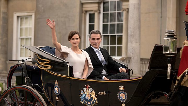 Kate and Hal in a carriage, her waving in a dress and him smiling in a scene from The Diplomat on Netflix.