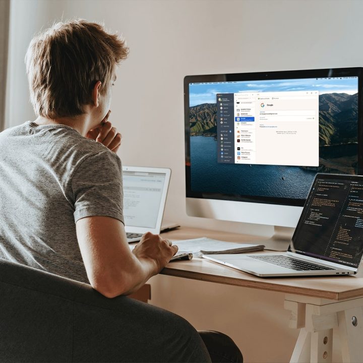 A person using 1Password on a desktop all-in-one computer while sat at a desk. There are two laptops next to them on the desk.