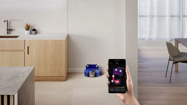 The Dyson 360 Vis Nav in its dock with the owner holding up a smartphone with the Dyson app.