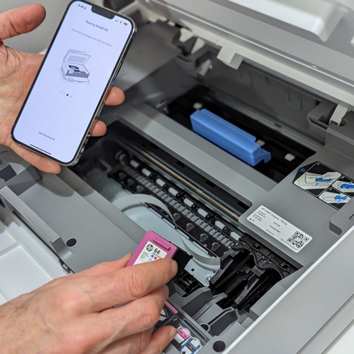 Installing ink cartridge in an HP Envy Inspire 7955e while referencing the HP Smart app.
