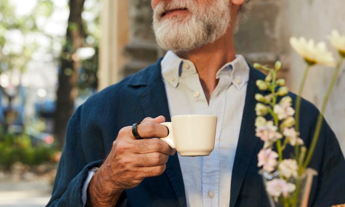 A man wears an Oura Ring Gen3 while drinking coffee at a cafe.