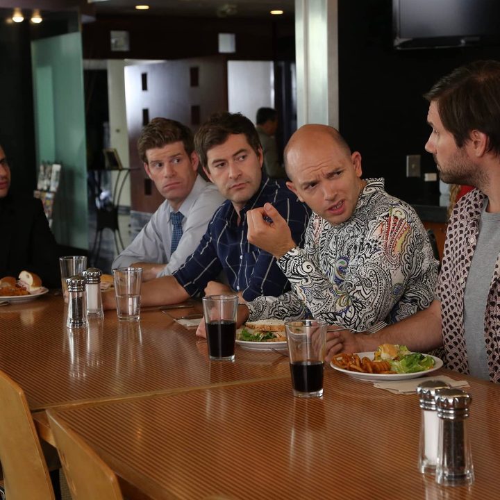 Five guys sit at a table and converse in The League.
