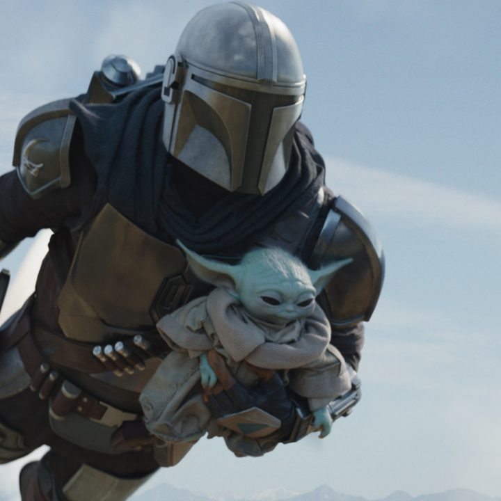 Din Djarin flying while holding onto Grogu.