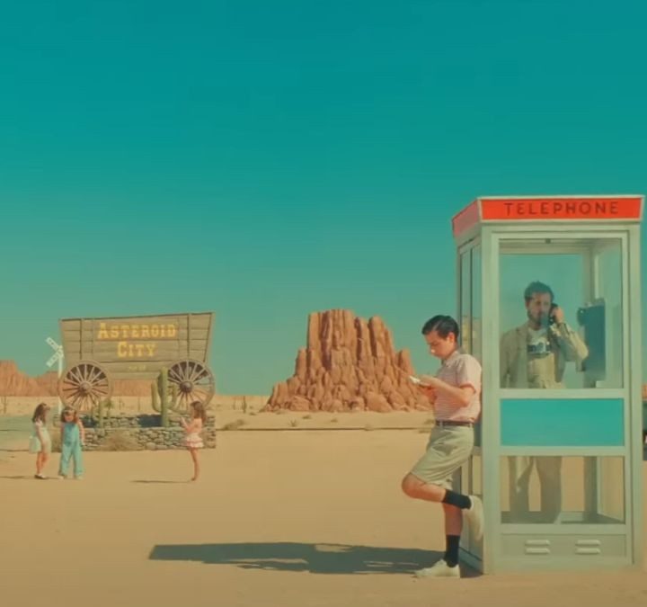A boy leans against a telephone booth in Asteroid City.