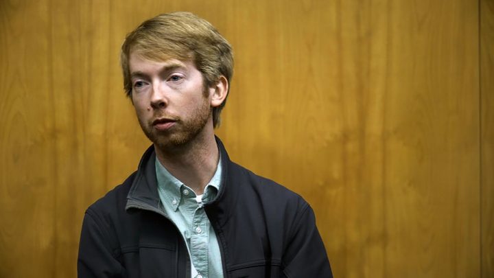 Todd standing in the courtroom looking over at someone or something in a scene from Jury Duty.