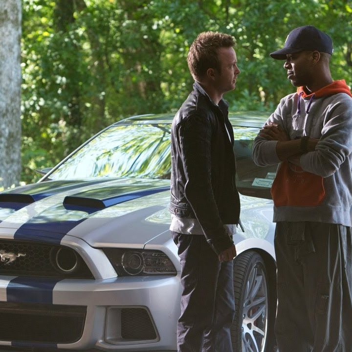 Two men talk in front of a car in The Need for Speed.