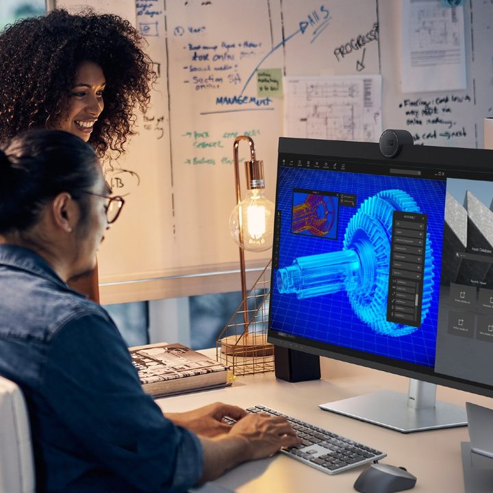 Two people using the Dell 6K Ultrasharp monitor on a desk.
