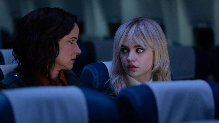 The present day and teen Natalie sitting together on a plane looking at one another in a scene from Yellowjackets.