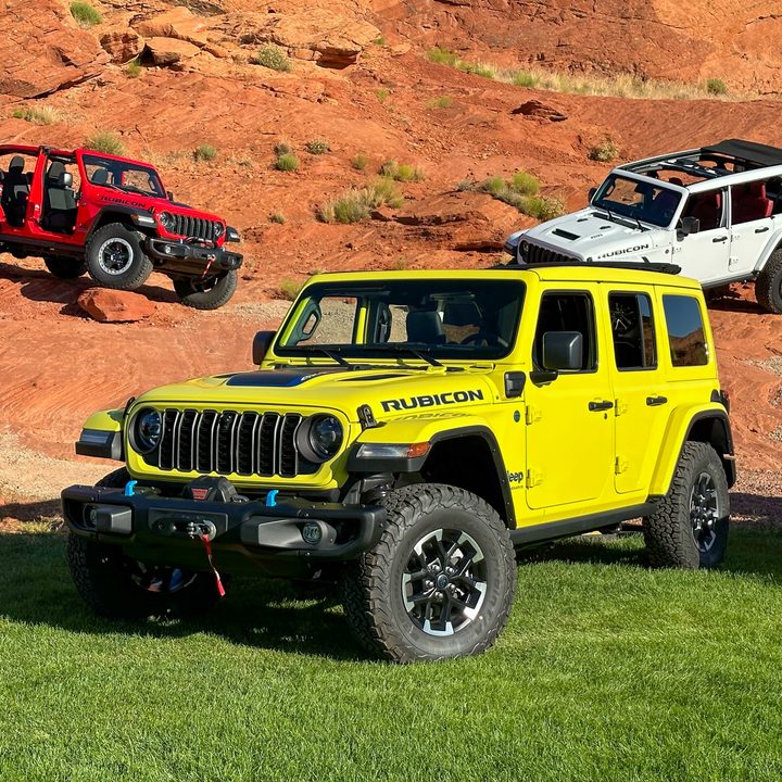 Three Jeep Wrangler 4xe SUVs on grass and dirt.