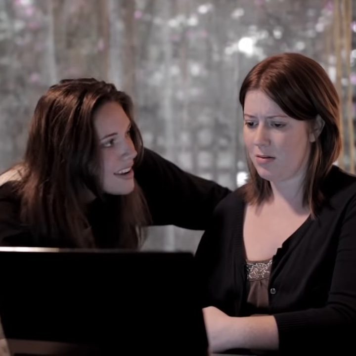 Two women gathered in front of a laptop in "Absentia."