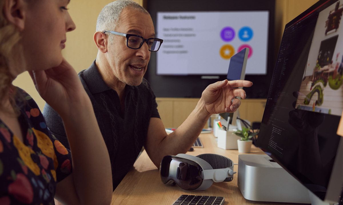 A developer points to a Mac screen while a Vision Pro rests on the desk.