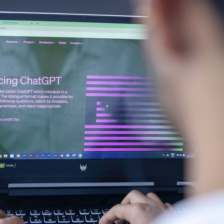 A person sits in front of a laptop. On the laptop screen is the home page for OpenAI's ChatGPT artificial intelligence chatbot.