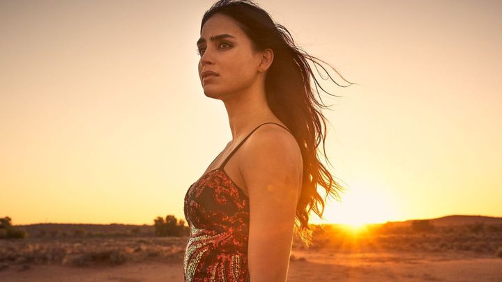 Melissa Barrera as Carmen looking to the distance with a sunset behind her in Carmen.