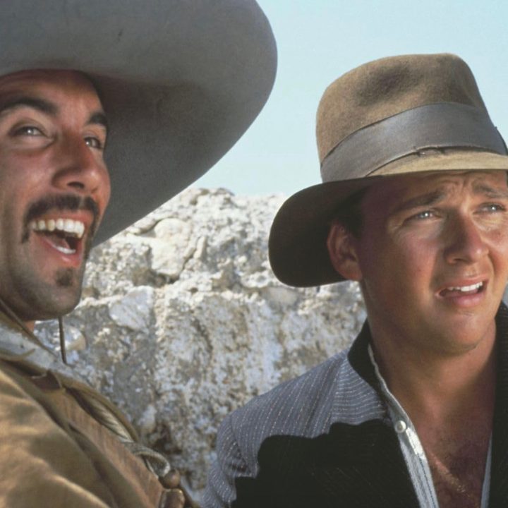 Indiana Jones and a friend stand next to each other and stare.