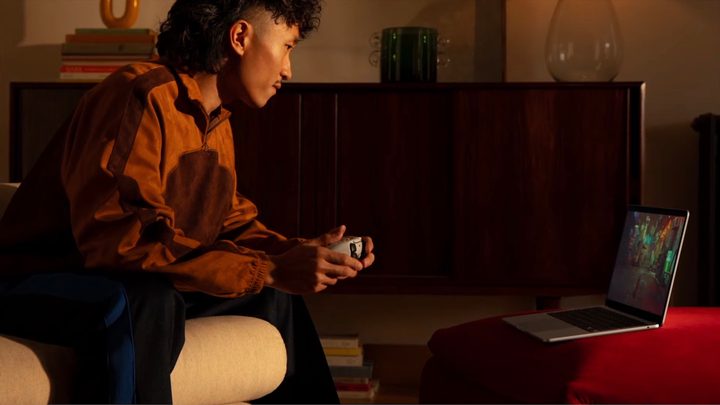 A person gaming with a controller on an Apple MacBook laptop.