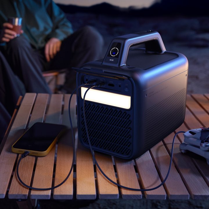 The Anker Nebula Mars 3 outdoor projector with its LED light on and devices charging off of it.