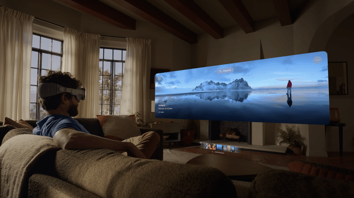A person sits on a couch looking at a virtual panorama via an Apple Vision Pro headset.