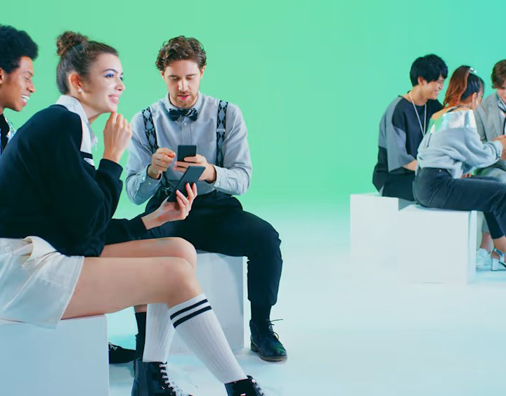 People sit on white blocks in a room holding smartphones.