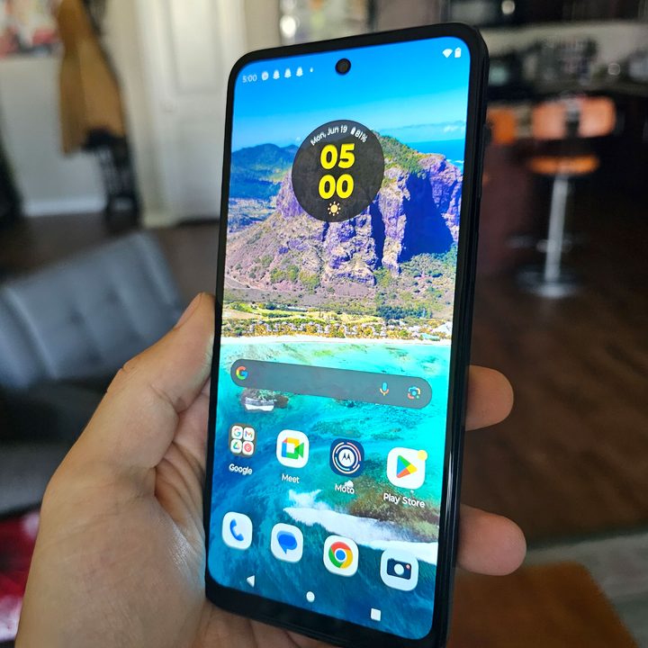 The Moto G 5G held in a hand with its screen illuminated.